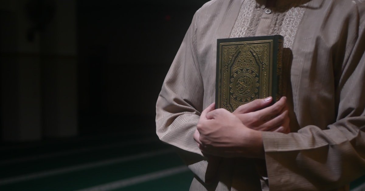 A person holding a gilded copy of the Quran close